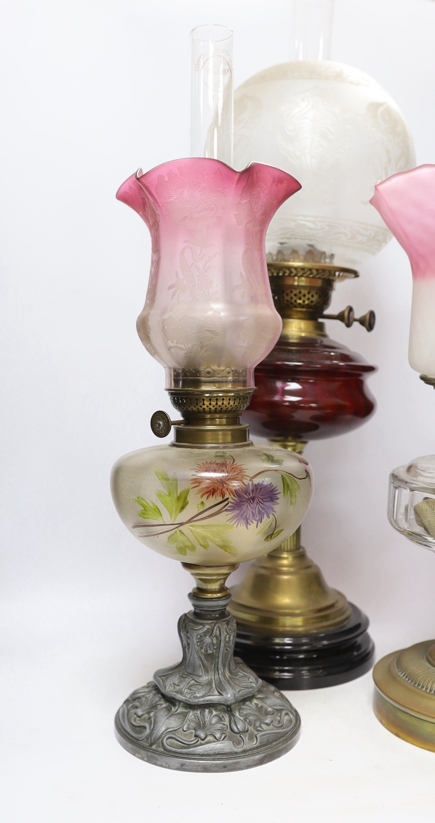 Three oil lamps with glass reservoirs and shades, one with Art Nouveau style base, 62cm high